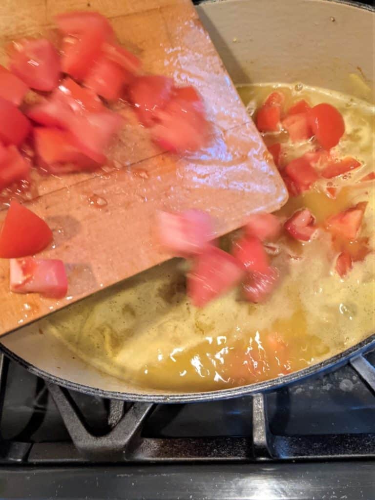 Adding chopped tomatoes to the Dutch oven to make delicious pregnancy soup.