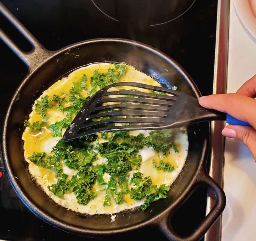 adding kale to the scrambled eggs in a skillet