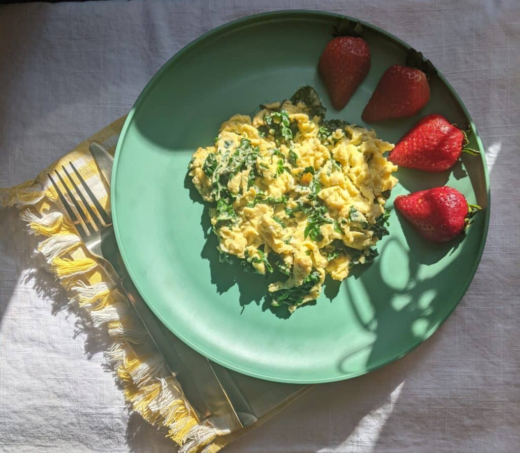 a plate of scrambled eggs mixed with kale on a green plate with strawberries
