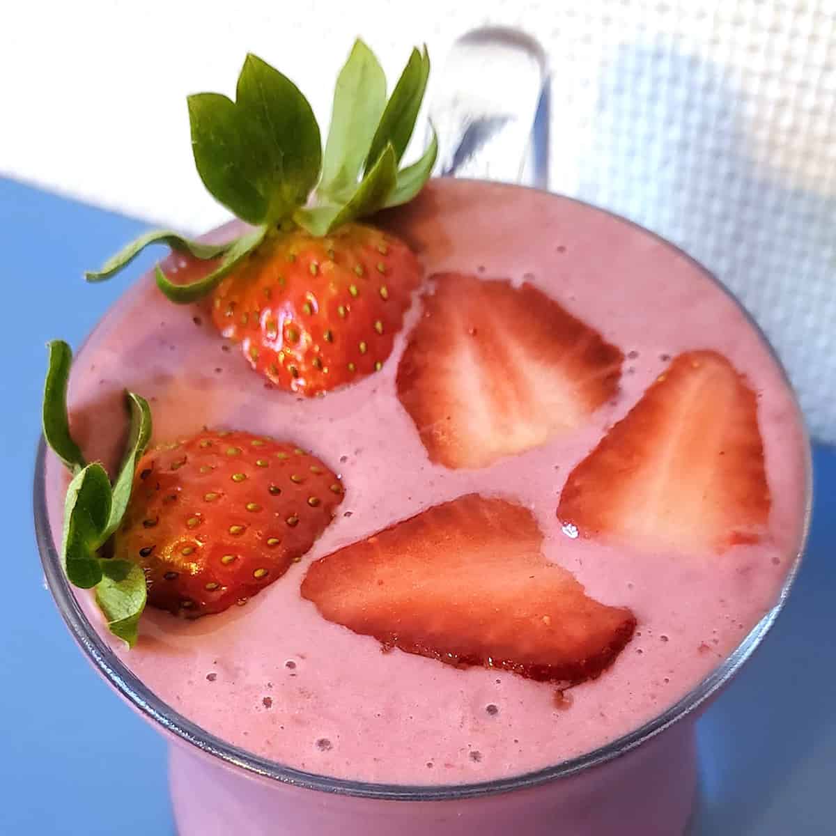 Smoothie in glass mug topped with sliced strawberries.